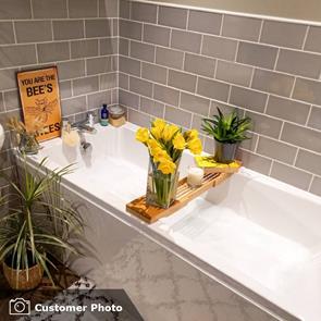 A bathroom fully tiled in savoy steel with a squre bath and oak plint resting a vase with yellow flowers.
