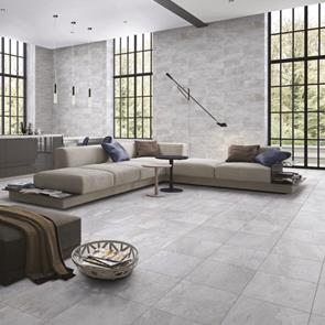 Open plan living room fully tiled with nature grey tiles, with the 500x500 floor tile and matching 690x240 on the wall with large floor to ceiling black framed windows