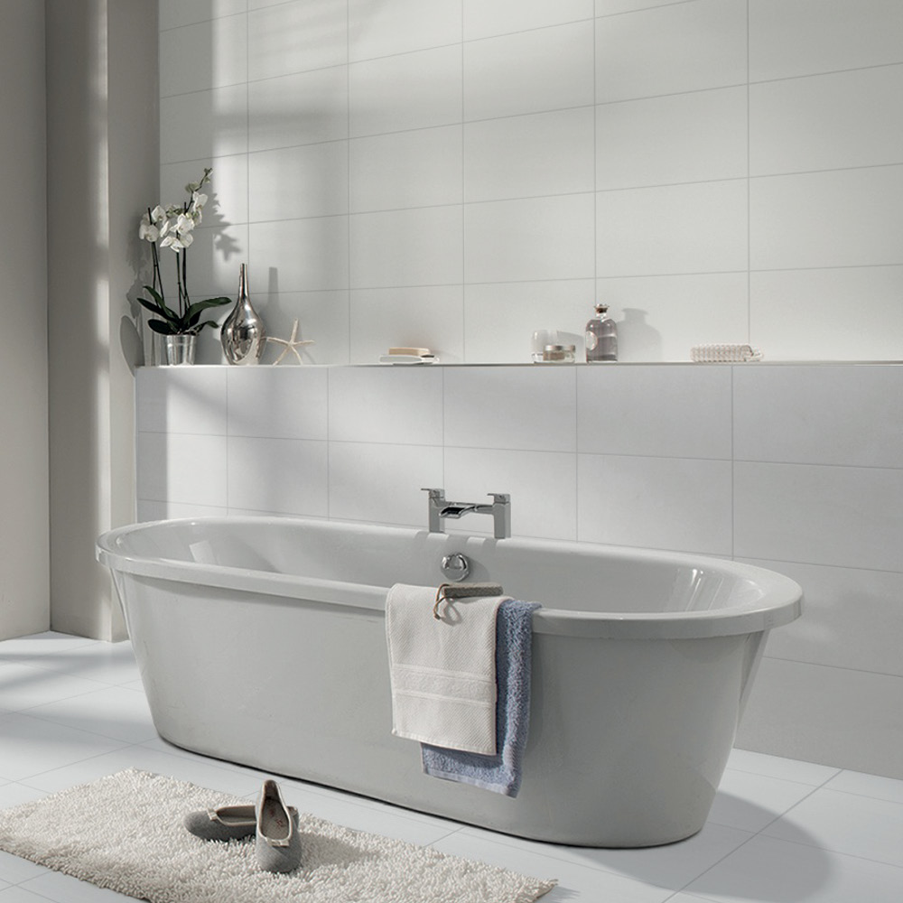 Freestanding gloss white bath in the centre of a bathroom, streamline natural white fully tiled behind.